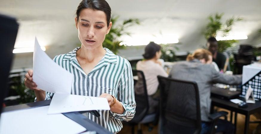 woman standing at printer holding a printed piece of paper