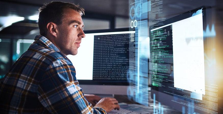 man looking at code on multiple computer screens