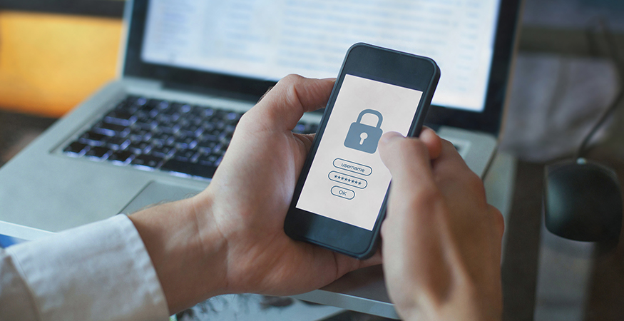 Person holding a smart phone with a lock icon on the screen in front of a laptop.