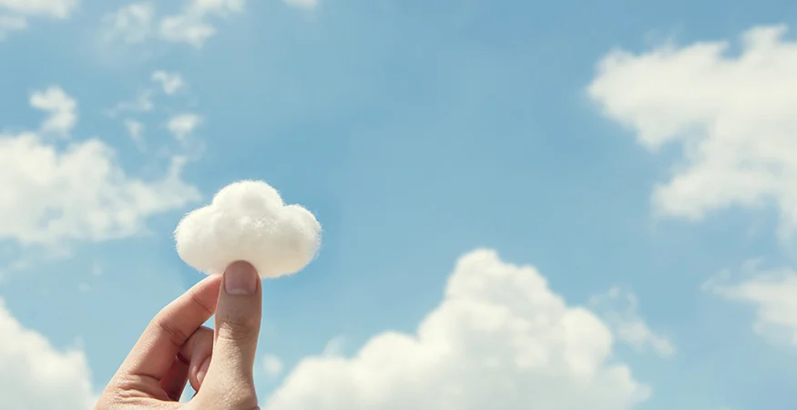 Hand holding cotton that looks like a cloud in front of other real clouds.